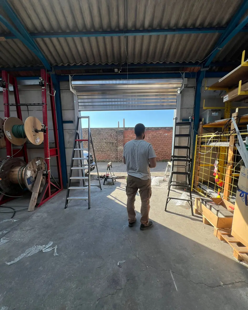 Serrurier de Bati Secure dans l’atelier, devant un volet de garage industriel en cours de pose
